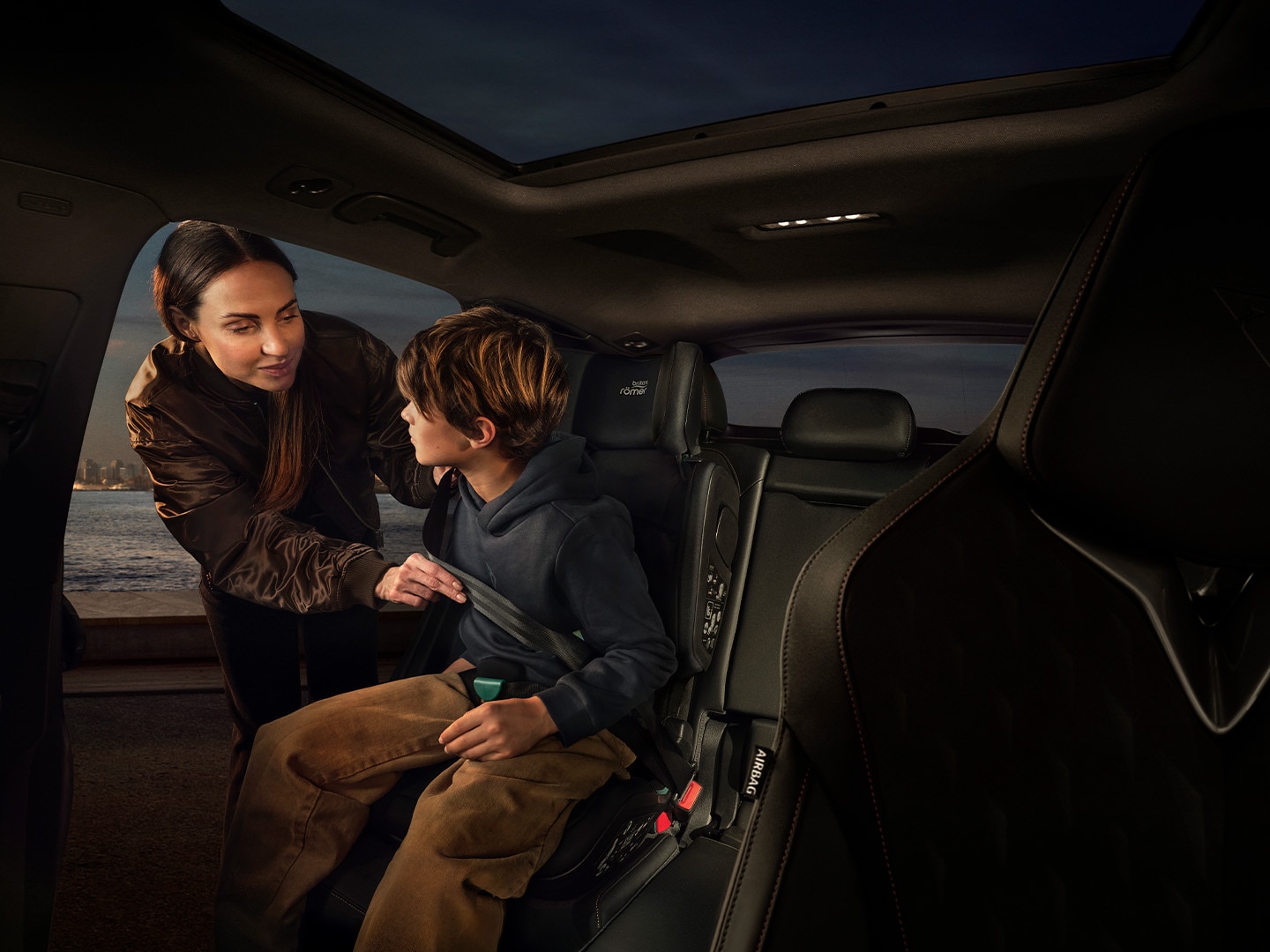 CUPRA Terramar interior view showcasing the backseat. There is a woman fastening the child safety seat to a kid.