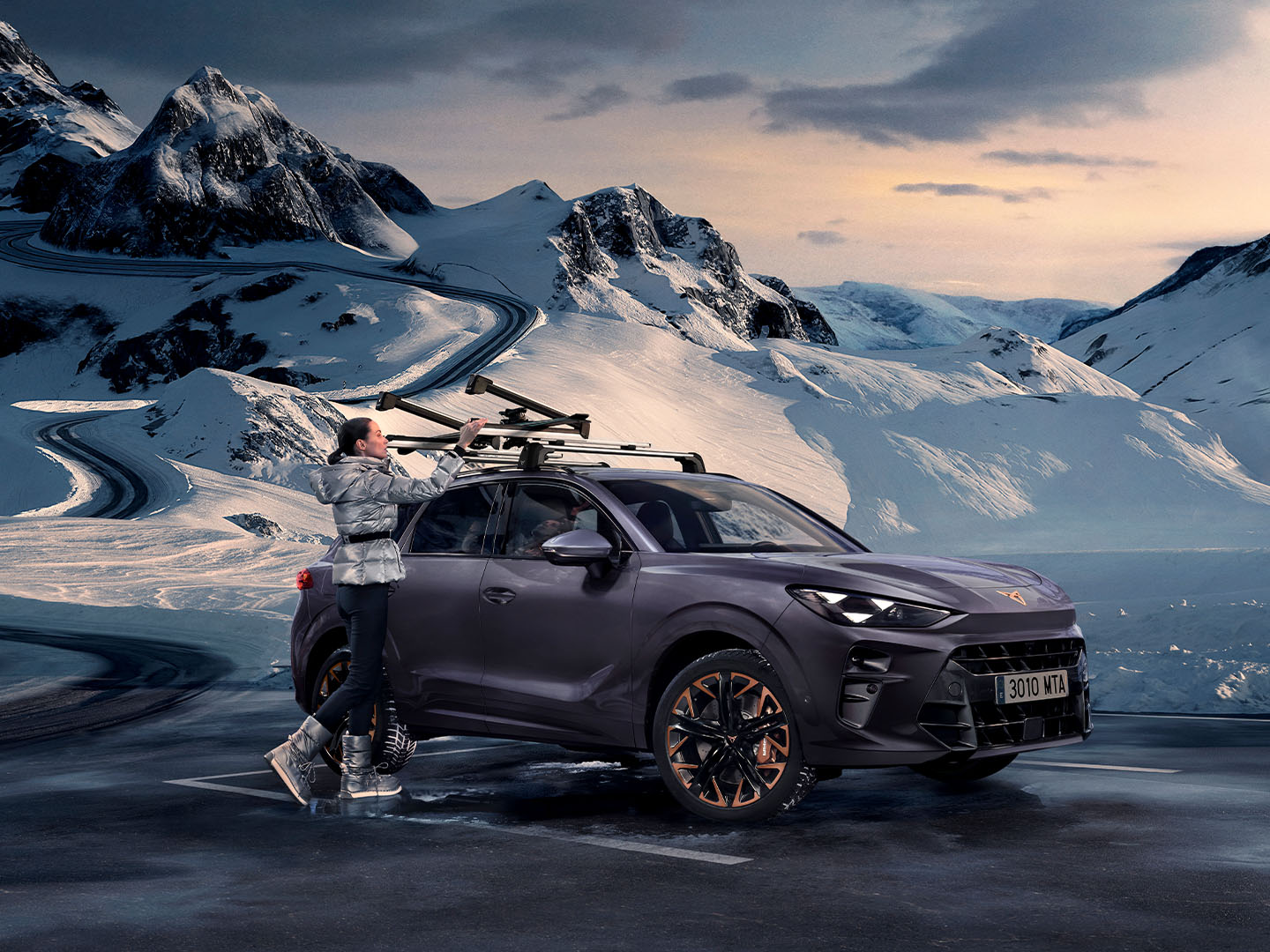 CUPRA Terramar in a snowy backdrop, showcasing the ski rack, one of its transport accessories, assembled on the roof. There is a woman using this rack for transporting its skis.